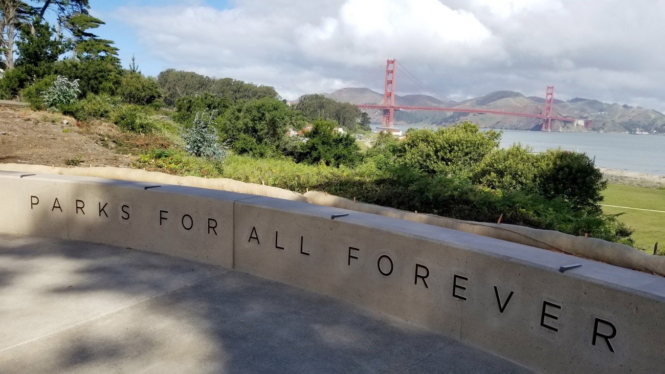 Cement seating area that reads "Parks For All Forever" with view of the Golden Gate Bridge in background