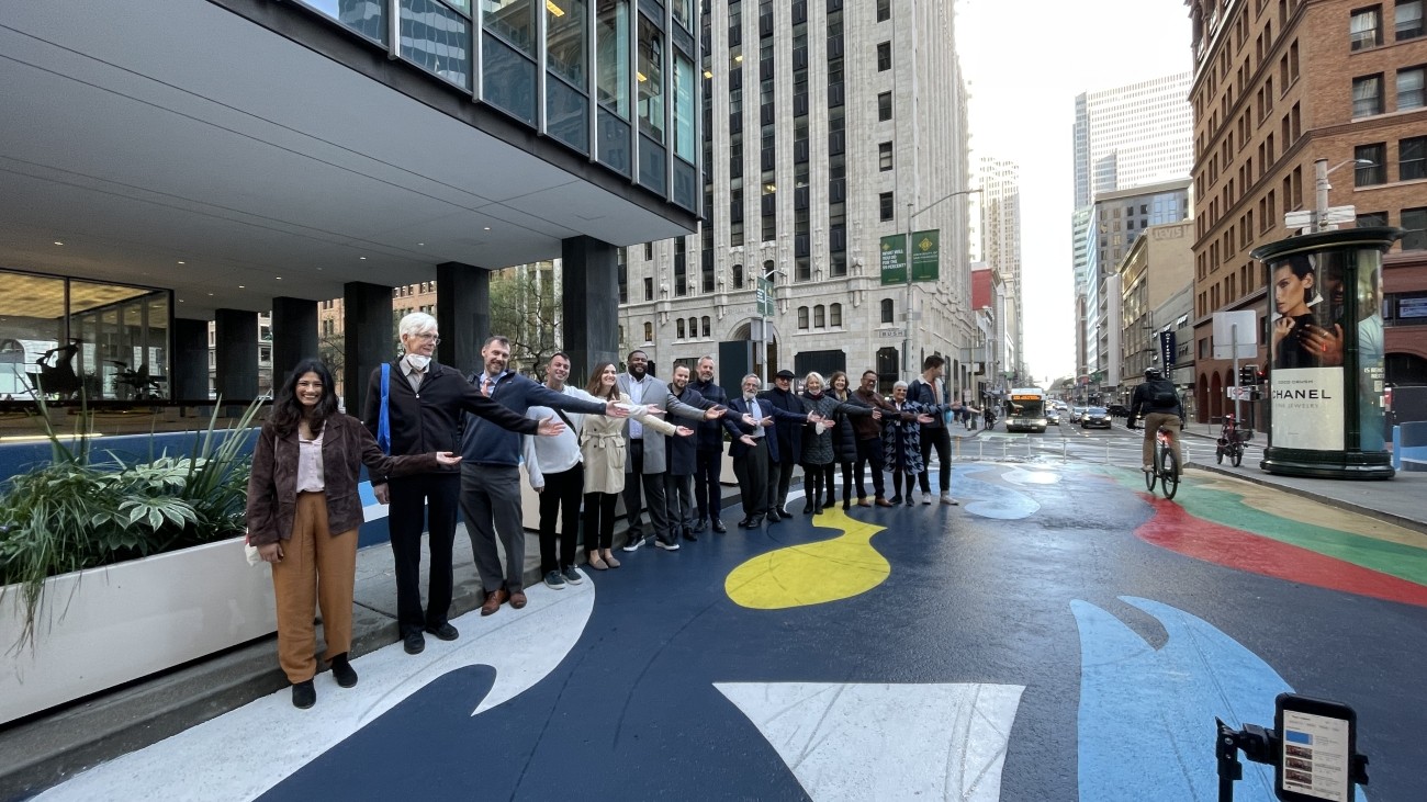 People standing in a line with arms out to show the mural painted on a protected bike lane