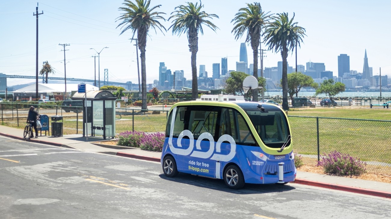 A Loop shuttle vehicle on Avenue B on Treasure Island. The San Francisco skyline is visible in the background.