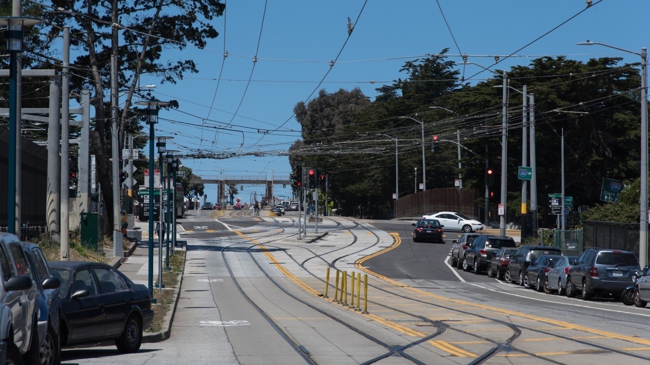 Pedestrian walking dog on crosswalk with vehicles and train approaching