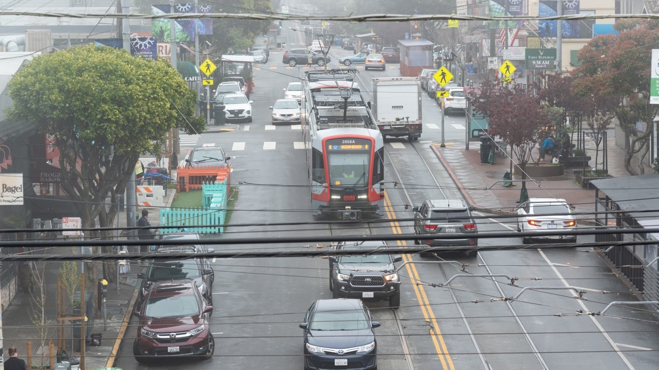 An N Judah streetcar crosses 9th Avenue at Irving in moderate traffic.