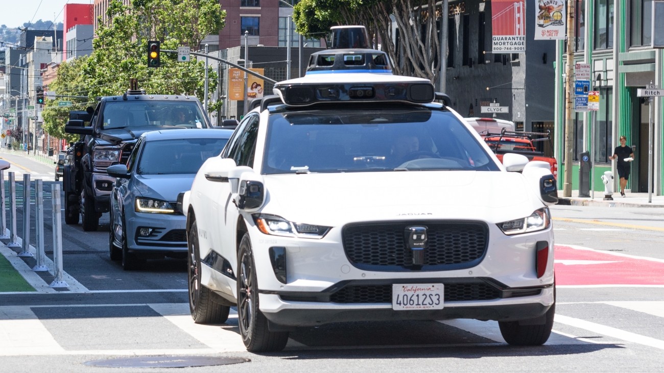 An autonomous vehicle drives through an intersection in SoMa, followed by two human-driven vehicles.