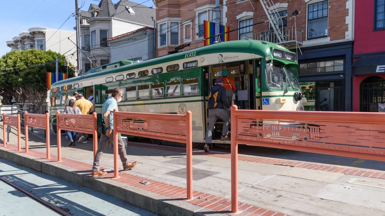 Orange "HOPE" themed railings along a transit boarding island with pedestrians Market Street with a green streetcar in the background