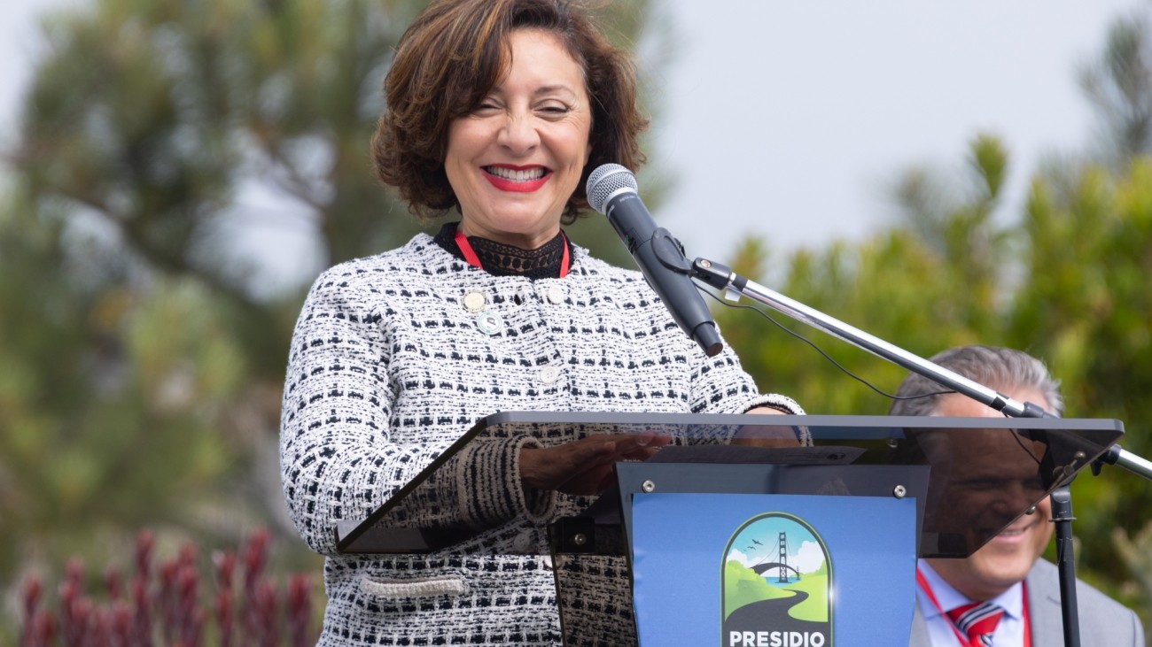 SFCTA Board Chair Myrna Melgar standing at a podium and smiling