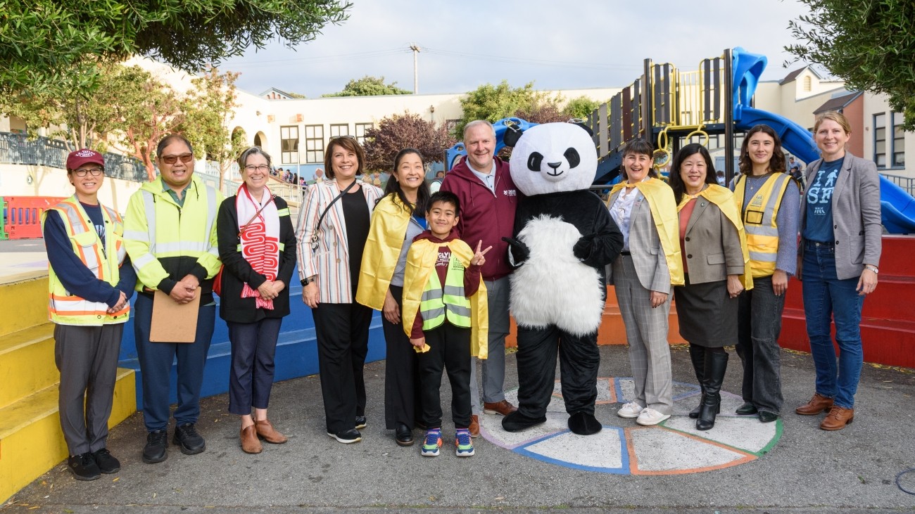Transportation leaders, community leaders, and school staff pictured together with a student and a panda mascot