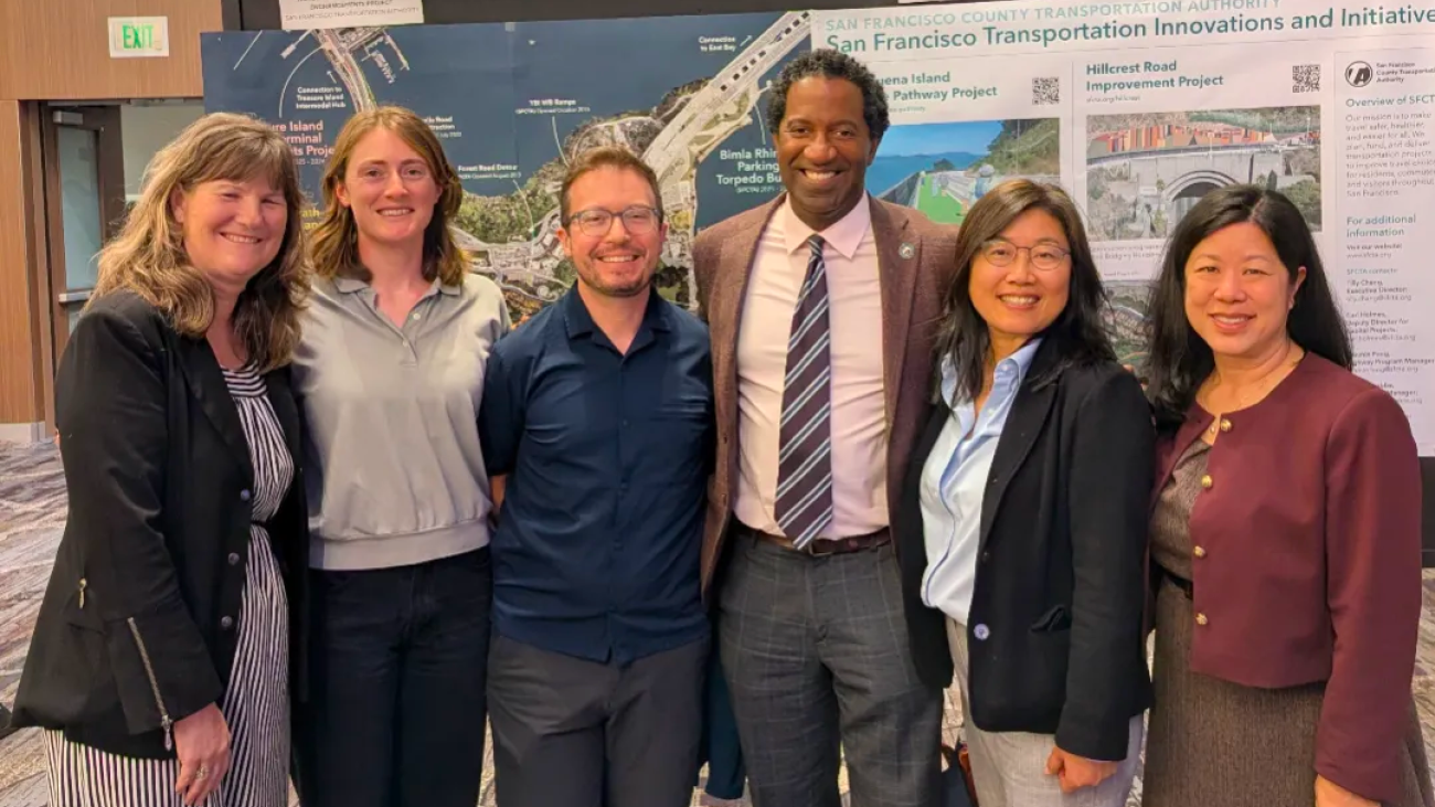 TA staff standing in front of the Yerba Buena Island poster