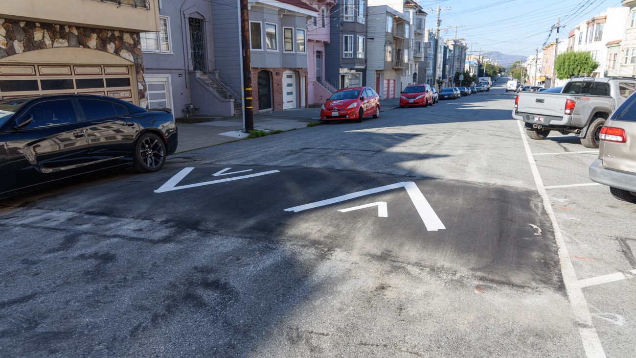 Speed hump with arrows and cars parked against the curb. 