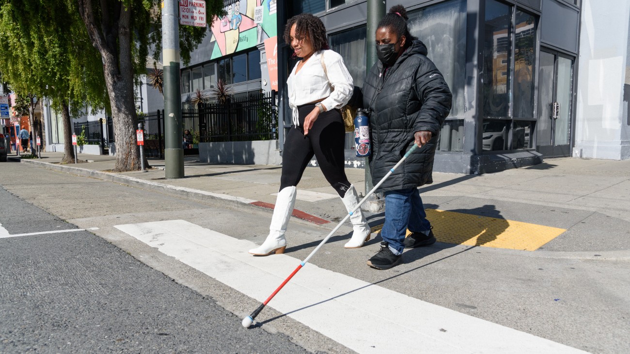 Visually impaired person & friend walking from curb ramp onto sidewalk