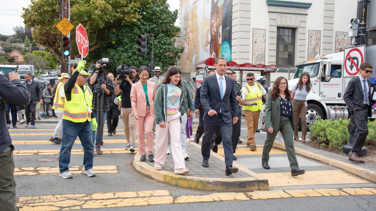 A group walking across the street with a school in the background 