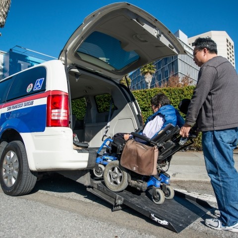 A taxi driver helping someone with a wheelchair get into a taxi