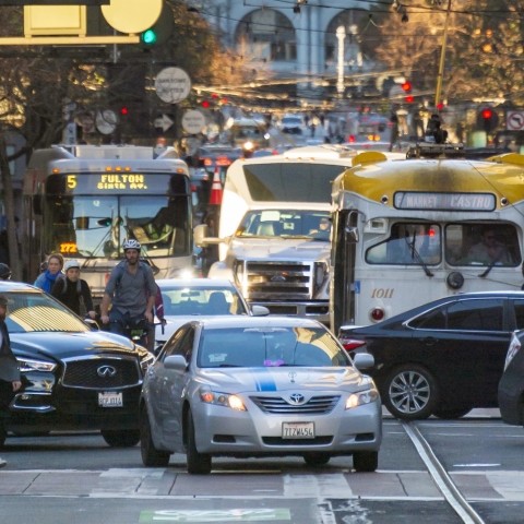 An Uber/Lyft vehicle among bicyclists, other cars, buses, and streetcars on Market Street