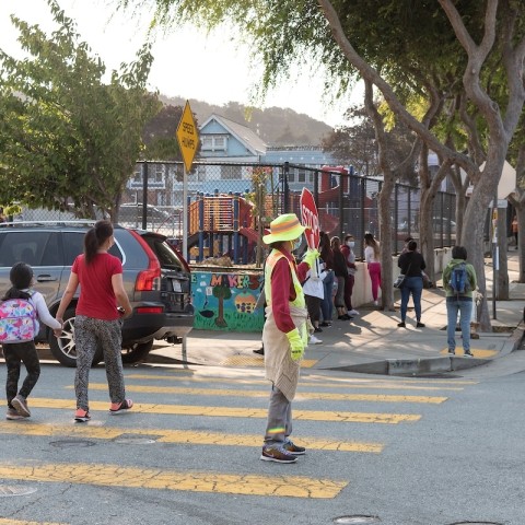 Crossing guard holding up a stop sign as parents and kids walk to school in the background.