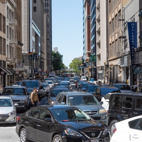 Many cars on a road with buildings in the background.