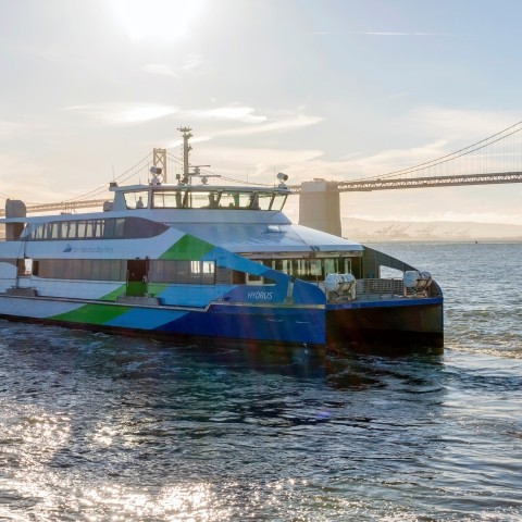 An SF Bay Ferry vessel cruises in front of the Bay Bridge. The early morning sun backlights the scene. Photo by Sergio Ruiz: flic.kr/p/2gbGJHK