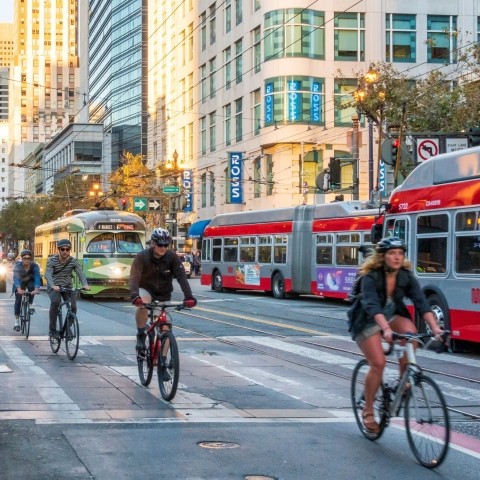 Bikers, buses, and cars traveling on a street in downtown San Francisco.