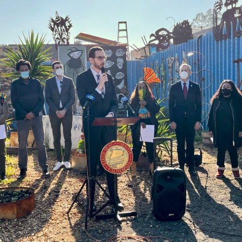 Senator Scott Wiener giving a speech in front of outdoor artworks as community leaders and transit officials gather behind him.