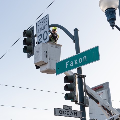 Worker installing a 20 mph sign on traffic post at Faxon and Ocean