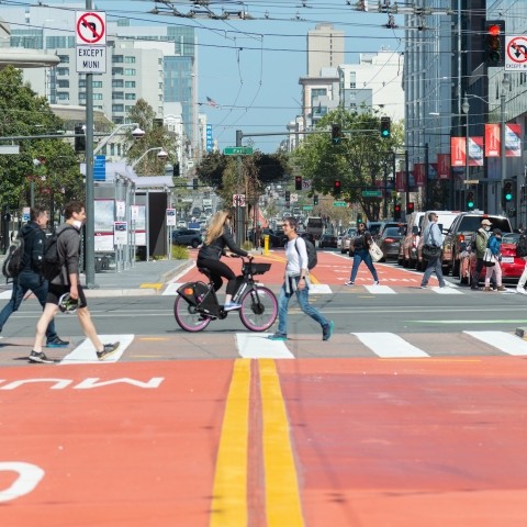Red transit lane with pedestrians and wheelchair user in crosswalk, cyclist riding adjacent to pedestrians