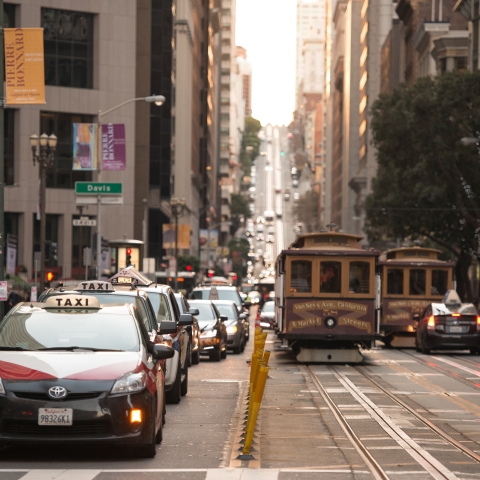 Taxis, vehicles, and cable cars on road with a pedestrian crossing in intersection