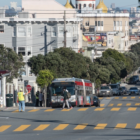 Cars and Muni bus on the road, crossing guard and youth in crosswalk