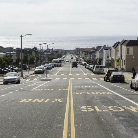 Ortega Street looking west toward the Pacific Ocean. "Slow school xing" is stenciled in yellow letters on the pavement. 