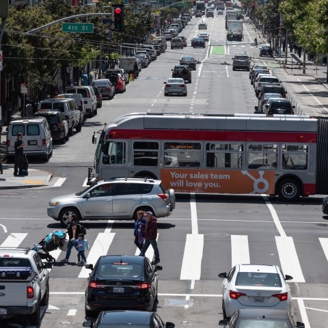 Muni buses, vehicles, and pedestrians on road along 4th Street