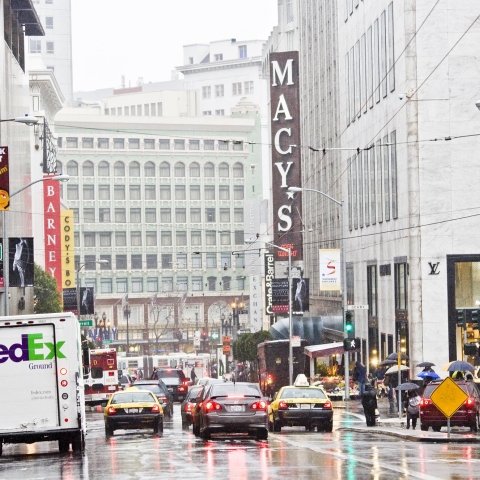 Vehicles and a Fedex truck along Stockton and Geary Streets. Market Street and Macy's signage visible in the distance. 
