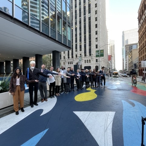 People standing in a line with arms out to show the mural painted on a protected bike lane