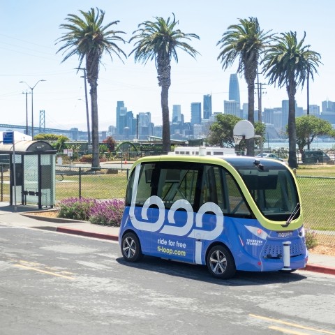 A Loop shuttle vehicle on Avenue B on Treasure Island. The San Francisco skyline is visible in the background.