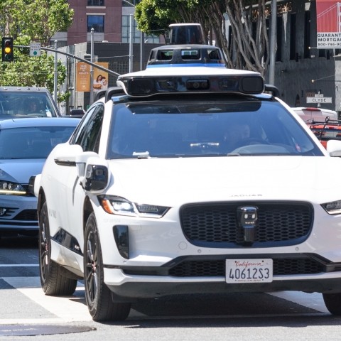 An autonomous vehicle drives through an intersection in SoMa, followed by two human-driven vehicles.