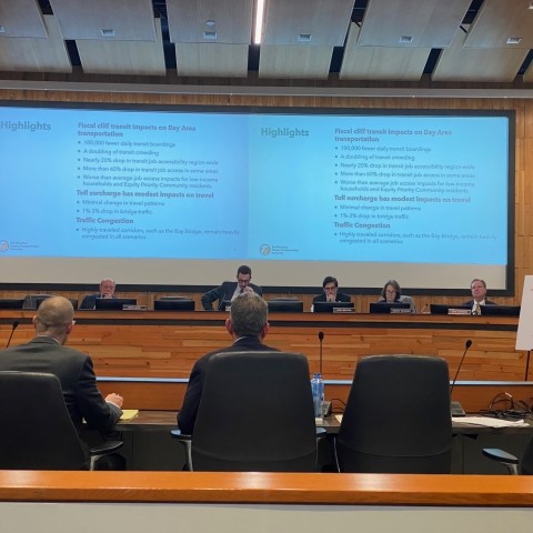 Government officials sitting in a board room with a presentation on screen