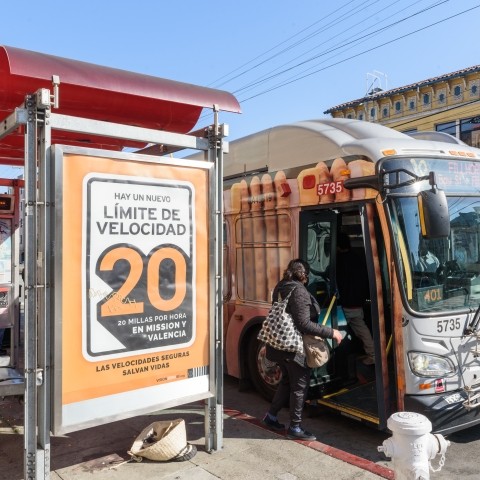 Vision Zero SF bus ad in Spanish showcasing the new reduced speed limit of 20 miles per hour. One individual is entering the bus