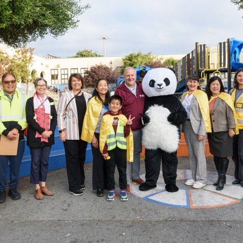 Transportation leaders, community leaders, and school staff pictured together with a student and a panda mascot