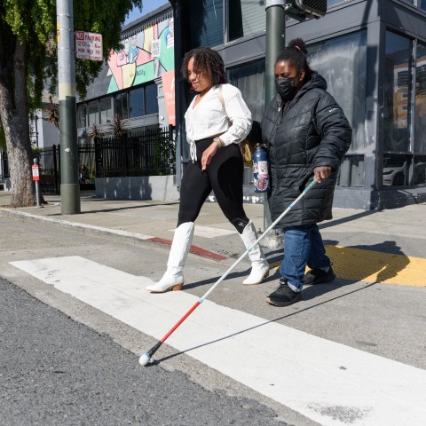 Visually impaired person & friend walking from curb ramp onto sidewalk