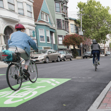 Bicyclists riding along street with green sharrow painted on road
