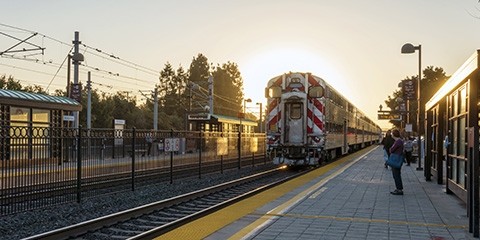 A train waits at the Mountain View Caltrain station, with the sun setting behind it.
