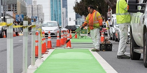 A worker applies green thermoplastic to a bike lane.