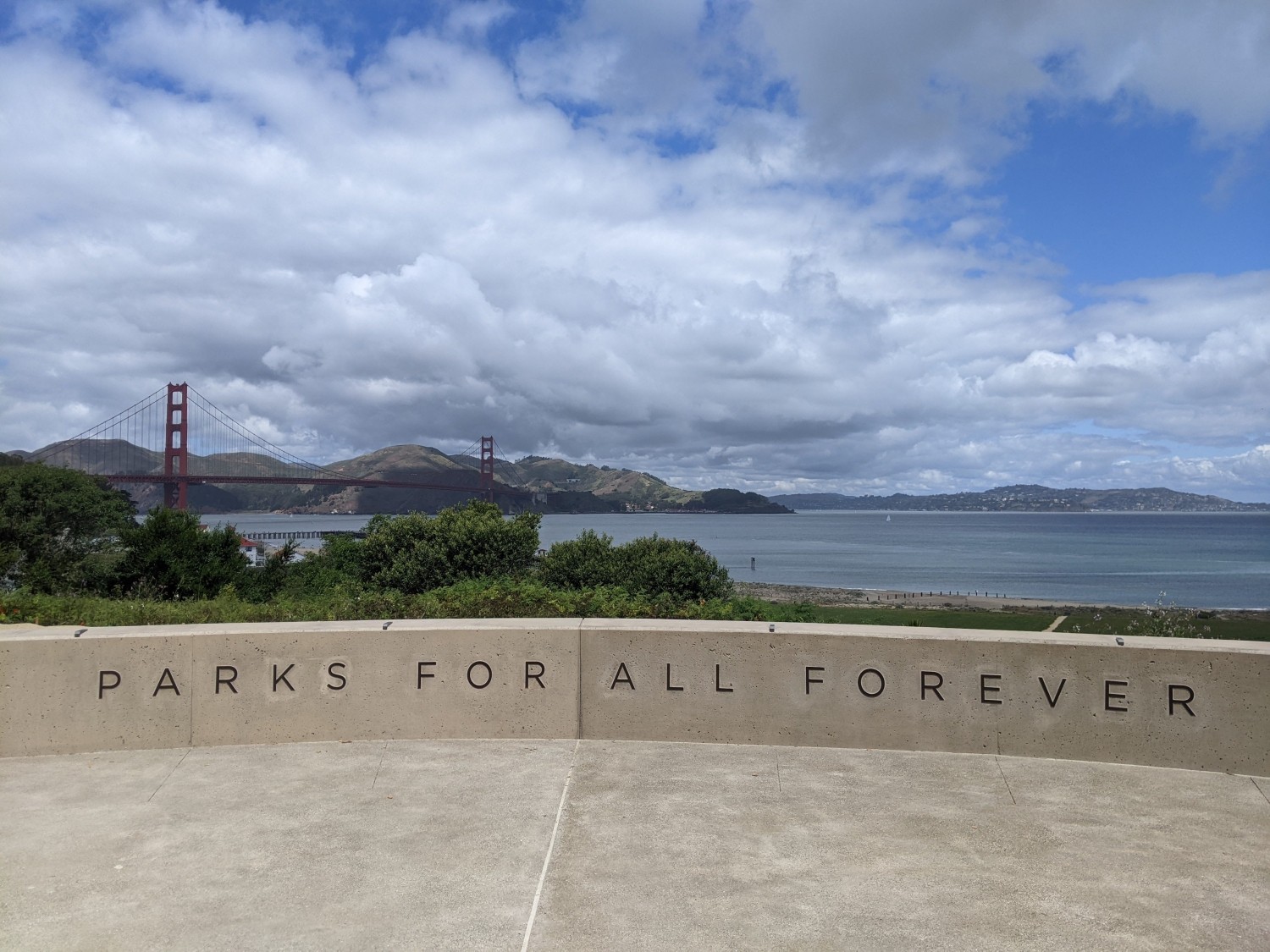 View of Golden Gate Bridget and water in background, with seating area that read 'parks for all forever'