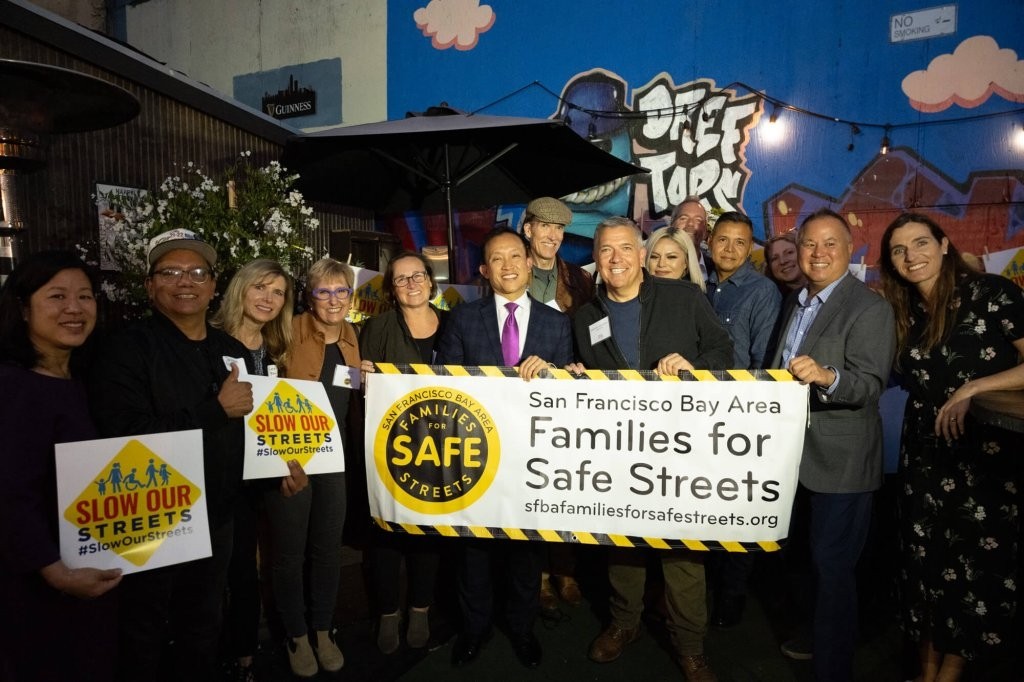 Transit stakeholders, elected officials, and community advocates pose with signage supporting safe streets. 